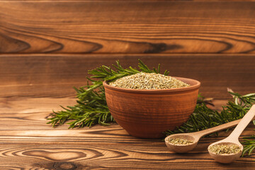 Fresh rosemary and dry spice in a plate and spoons on a brown textured background. Fresh spice herbs. Seasoning for meat and fish. Recipe.Organic bouquet of fresh rosemary on the table.Place for text.
