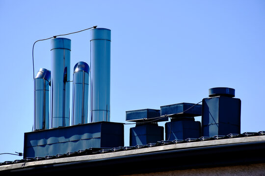 shiny stainless steel sheet mechanical air pipes, vents and ducts on flat roof. building engineering, heating, cooling and  building ventilation system. lightning protection and grounding. blue sky.