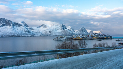 Panorama mit einer Insel mit einem Dorf im Fjord und den schneebedeckten Bergen von Norwegen. Fischerdorf Husøy auf Senja am Morgen im Winter