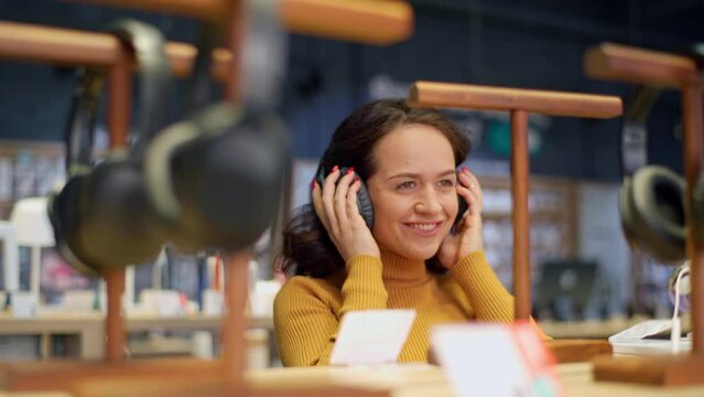 Attractive young girl with curly hair in an orange sweater is trying on headphones and enjoying music