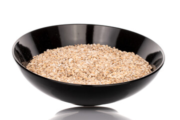 Organic uncooked pearl barley in a black ceramic plate, close-up, isolated on white.