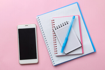 Notebooks pen and smartphone on a delicate pink background. top view
