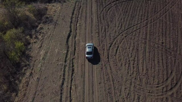 Aerial top view of grey car drives alone off-road on dirty rural roads filming by drone.