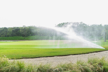 Automatic and technological sprinkler system on a green lawn, in the background the tropical trees and the sunlit sky in Mexico