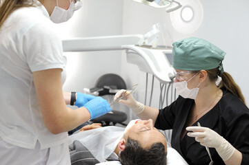 Surgery in a dental clinic. The dentist surgeon stitches the wound in the patient's mouth. stitch...