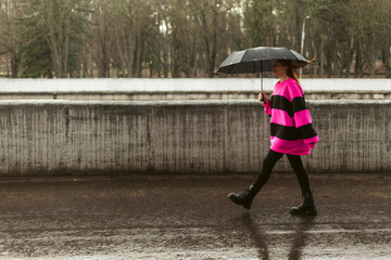 Woman in bad rainy weather walks the street. Bright Purple outfit. City landscape in rainy weather. City scenes in the rain.