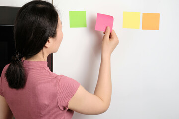 Oriental young woman sticking multicolored generic reminder notes onto fridge in house
