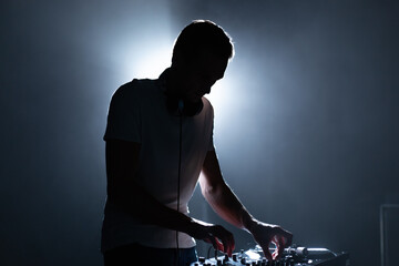 Silhouette of a DJ performing on party in night club. Cool young man playing music on stage