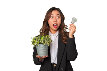 A young Chinese businesswoman holds a lightbulb and plant, embodying her innovative ideas and commitment to sustainability and the environment.