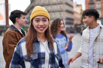 Chinese friend beaming with happiness, as diverse group chats and laughs in background, starting their Spain adventure.
