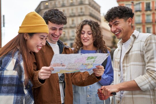 A diverse group of friends laughing and planning their Madrid sightseeing adventure with a city map in hand.