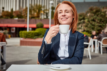 Taking a moment to recharge, a successful middle-aged businesswoman enjoys a peaceful coffee break on a sunny terrace.