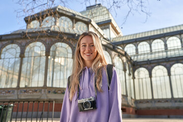 Young caucasian woman captures joy of travel with her camera in front of the crystal palace in Madrid