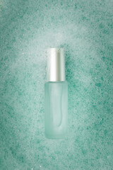 Elegant cosmetic serum glass bottle in pastel blue foam with bubbles. Minimal surreal design. Bright foamy background.