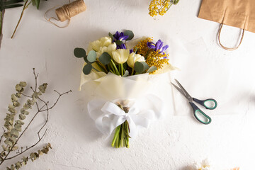 Make bouquet florist workplace. Flower arrangement in a flower shop. Spring bouquet of yellow flowers. Irises, tulips, mimosa and eucalyptus. Tulip bud. Floral background. Purple iris. White table