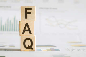 FAQ concept on wooden cubes and financial graphs in the background