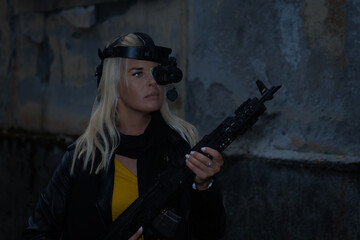 Fototapeta na wymiar Warrior girl with a night vision device and an assault rifle near an abandoned building at night.