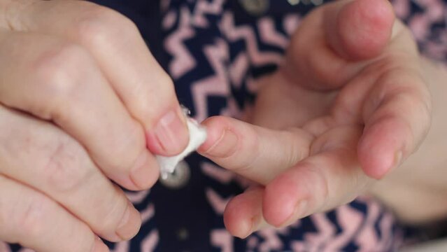 hands of a diabetic woman wiping blood from her finger with a cotton swab after a glucometer test. woman checks blood sugar at home.