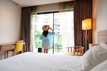 Young Asian traveler woman with luggage and straw hat in hotel room after check-in. Travel and summer holiday concept. Copy space