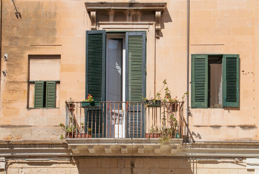 Tradicional balc&oacute;n en las estrechas calles de Lecce, Italia. Balc&oacute;n con macetas y las contraventanas de madera abiertas rodeado de dos peque&ntilde;as ventanas de dise&ntilde;o tradicional.