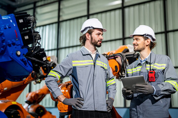 Engineer explaining to controlling robotic welding process to welder in factory.