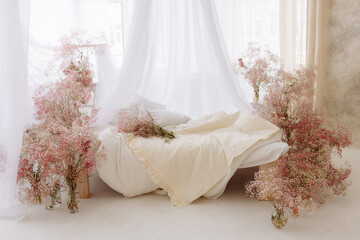 Elegant cozy bedroom in soft light colors, a large comfortable double bed with a canopy decorated with bouquets of gypsophila flowers in vases