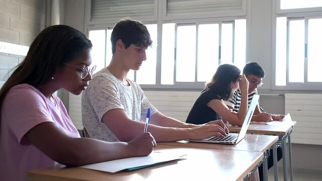 Teen female black high school student doing homework in class with other multiracial classmates. Handheld 4k video.