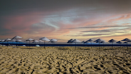 Empty lounge chairs and wicker umbrellas on beach. Nobody on long empty beach at seaside resort...