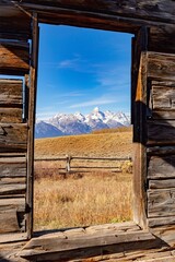 Abandoned deserted cabin window view of the autumn landscape and corral fence of the Grand Teton Range in Grand Teton National Park, Wyoming.