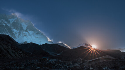 Landscape with sunrise behind snowy mountain with sunbeams and shadows across sky, Nepal, Himalayas