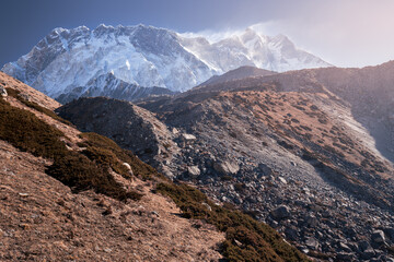 Sunlit mountain landscape with rocky hills in front of giant snowy wall of Lhotse, Nepal, Himalayas