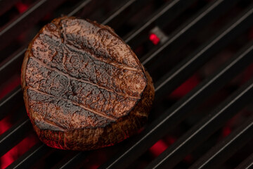 A juicy steak sizzling on a cast iron grill over a flame. The steak is perfectly cooked and has grill marks. The background is dark and smoky