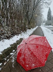 Close up of red umbrella in snow with frost and snowflakes. Street and the first snowfall of the winter season