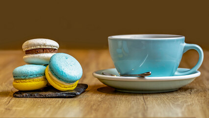 Macaron cakes and a blue cup with tea on a brown background.
