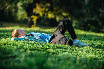 Young cheerful child relaxing in a park. Smiling child laying down on the grass in a garden and...