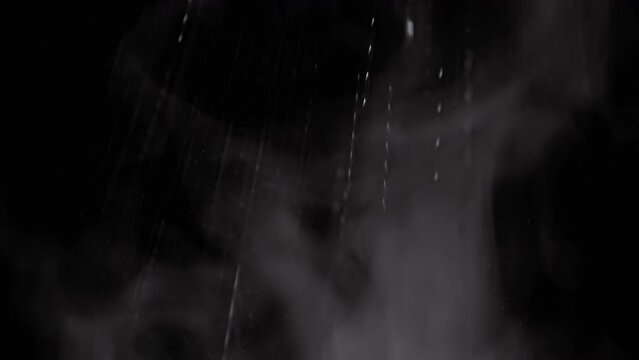 Falling Stream of Splashes on a Rising Cloud of Water Vapor on Black Background. Explosion of mixed particles of dust, gas, smoke, snow. Icy cloud of steam, drops of water swirl in whirlpool. Storm.