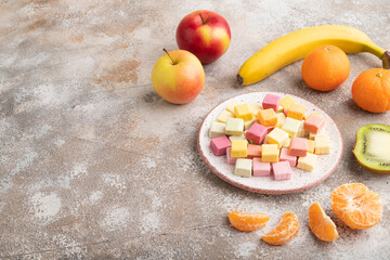 Various fruit jelly chewing candies on brown concrete. apple, banana, tangerine, side view, copy space.