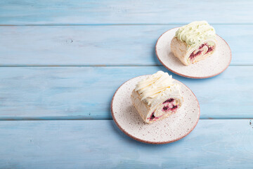 Roll biscuit cake with cream cheese and jam on blue wooden, side view, copy space.