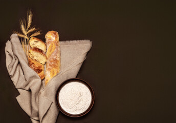 Baguette on a brown background with ears of wheat and flour