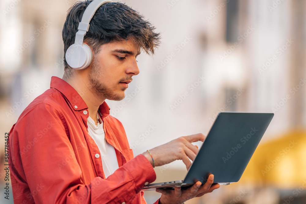 Poster young male with headphones and laptop in the street