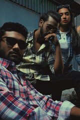 Two men and a girl sitting on a bench, one wearing sunglasses and the other wearing a plaid shirt