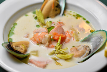 Mussels with king prawns in a creamy sauce with avocado and red fish in a white deep plate on a dark green background