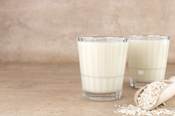 Two glass of oat milk and oatmeal on beige background. Copy space. The concept of alternative lactose-free dairy products.