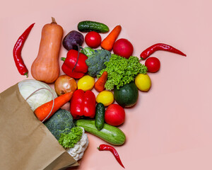A set of fresh vegetables in a paper bag on pink background