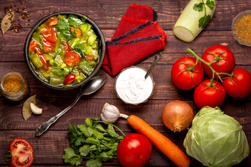 Plate with vegetable freshly prepared soup and vegetables on a wooden table close-up.