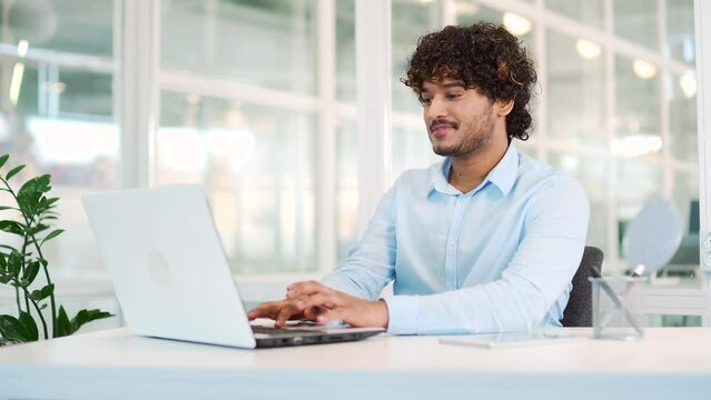 Young smiling employee has a good idea while working on a laptop while sitting at the workplace at desk in a modern office. Happy handsome worker rejoices because he found a solution to the problem