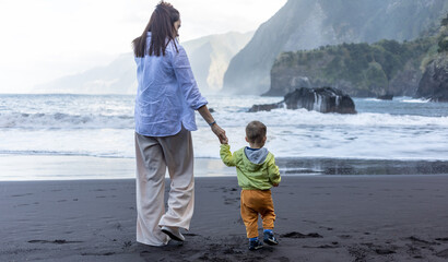 Mother and little child holding hands walking at sea side - 587790494