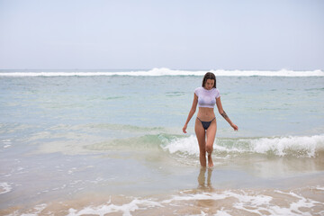 Fototapeta na wymiar Beautiful young woman in a white cropped t-shirt comes out of the ocean.