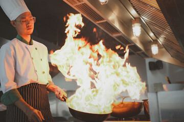 Chef in the restaurant kitchen making flambe on frying pan. Cooking food in a frying pan with fire. Chefs doing flambe on food..