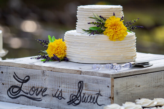 Love is sweet cursive rustic country style wedding cake with yellow flowers.